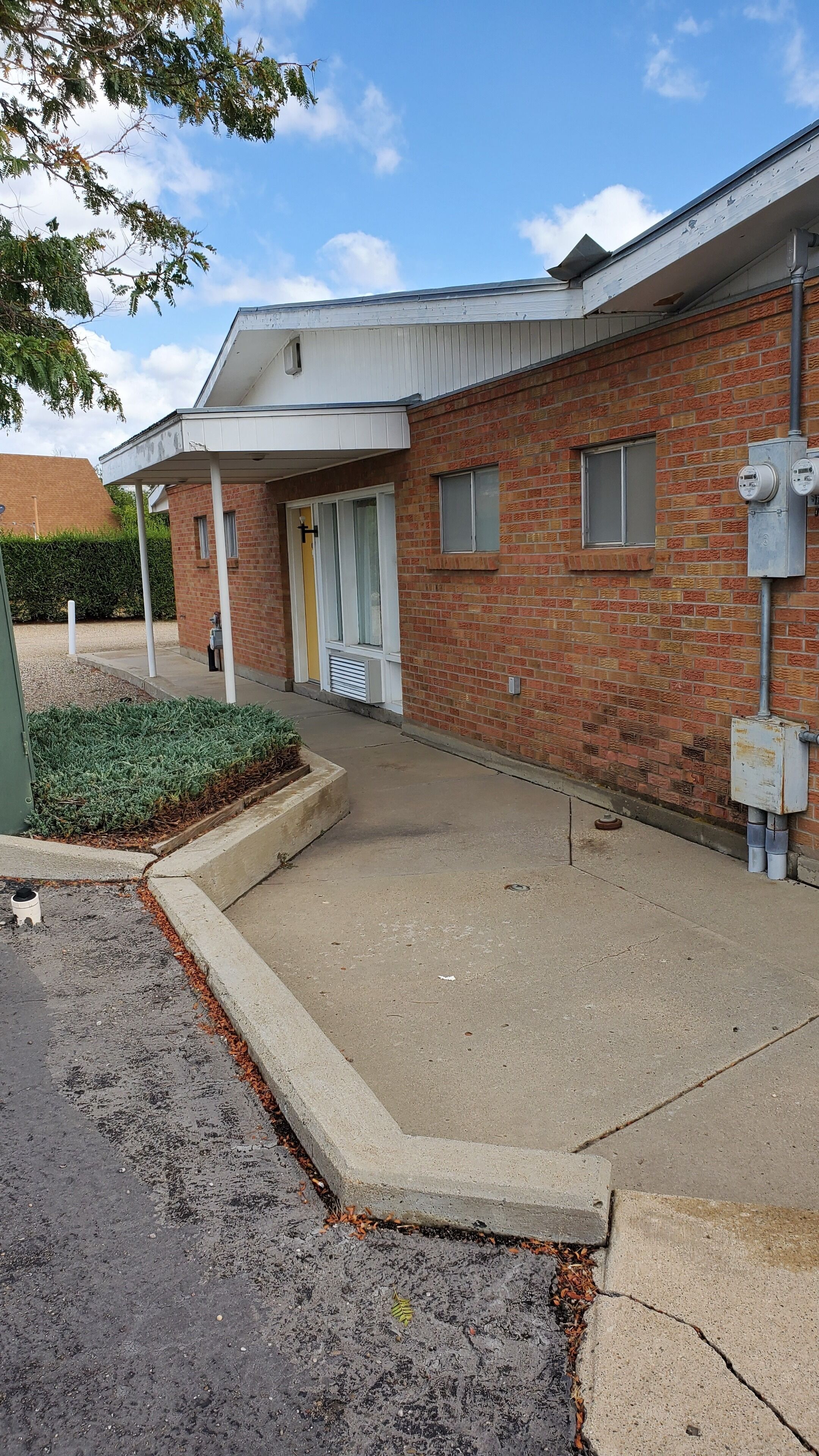 A two-story building with a brick facade, a covered entrance, and a small garden area.