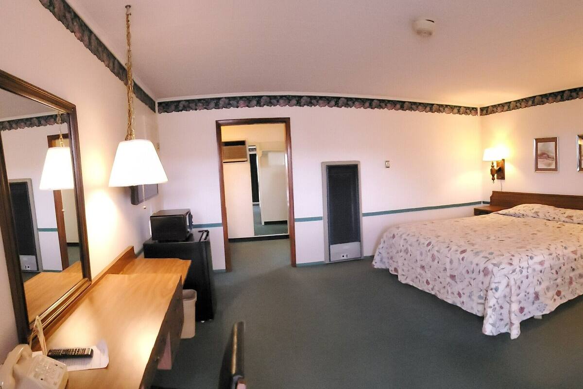 A hotel room with a bed, bedside table, chair, desk, mirror, and wall-mounted lamps.