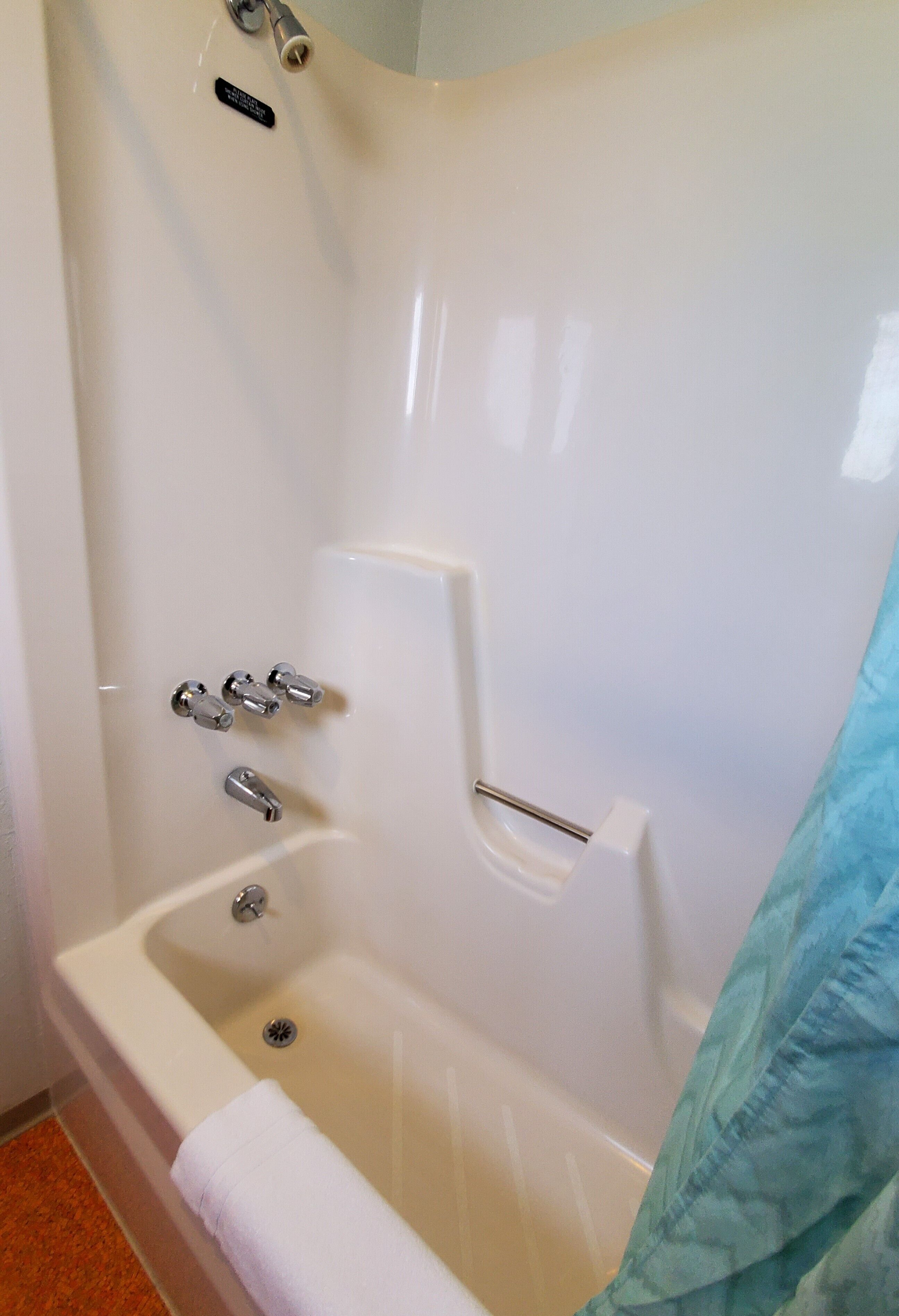 A white bathtub with a handheld showerhead, a built-in seat, and a towel rack.