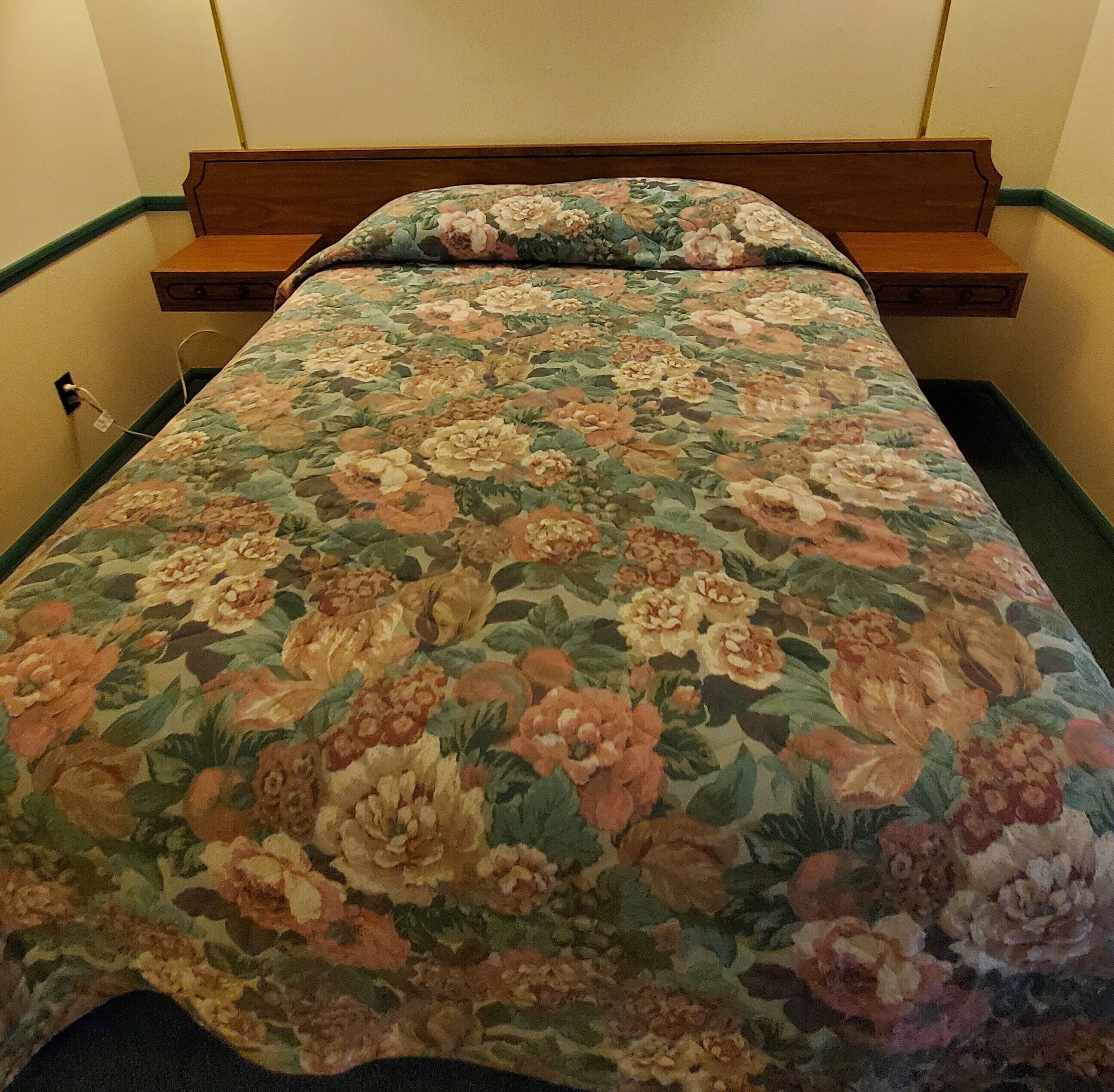 Un lit avec une couvre-lit à motifs floraux et une tête de lit en bois.