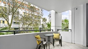 A balcony with two chairs and a small table, overlooking a building with trees and a clear sky.