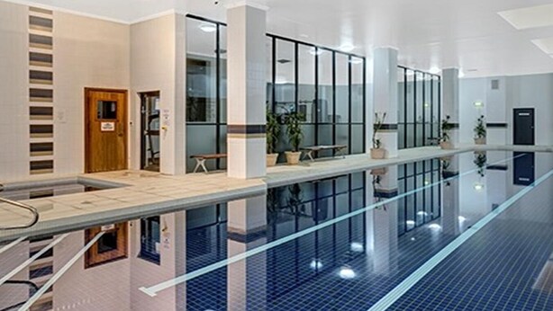 A modern indoor swimming pool with glass walls, a wooden door, and potted plants.