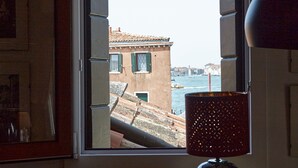A room with a window overlooking a cityscape, a table with a candle, a glass, and a bowl. - Acqua Susanna - Penthouse with terrace (Venezia)