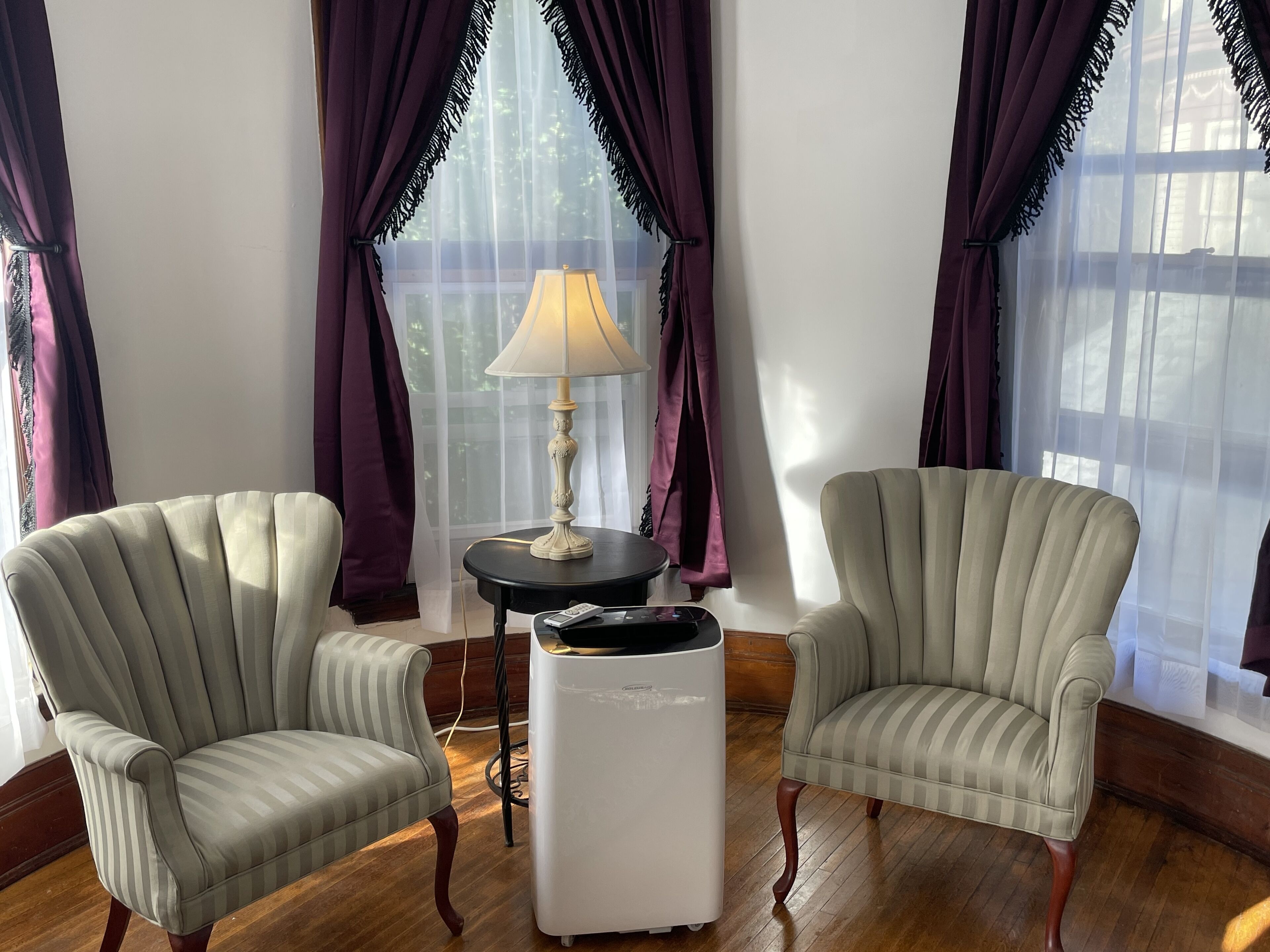 A room with two upholstered armchairs, a small round table with a lamp, and a white radiator.