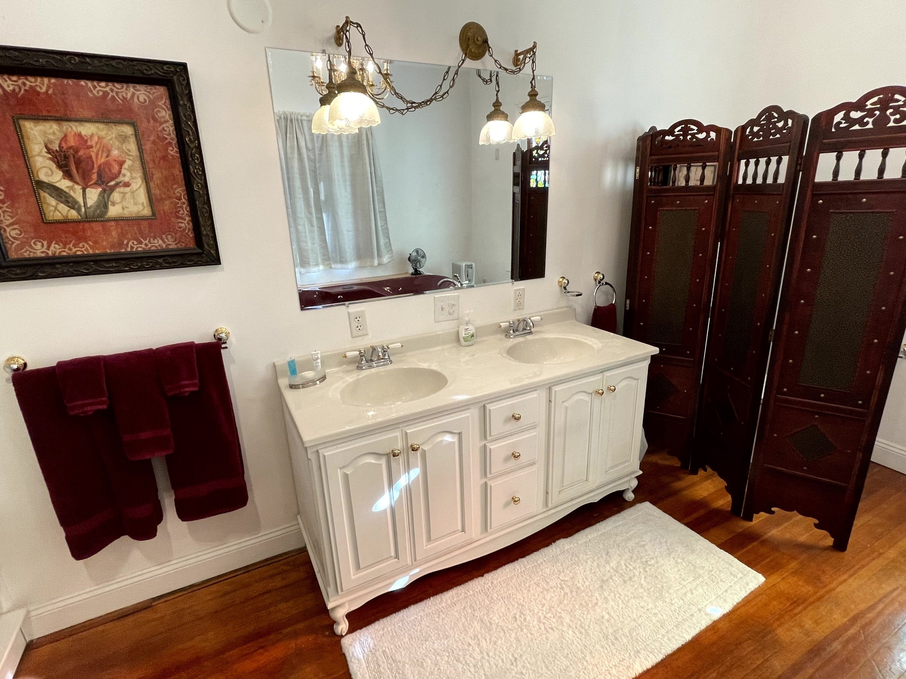 A bathroom with two sinks, a large mirror, a chandelier, and a red towel rack.