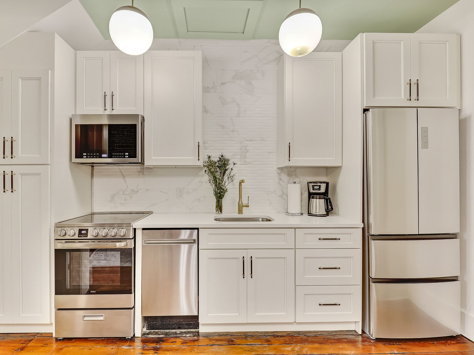 Una cocina moderna con muebles blancos, electrodomésticos de acero inoxidable y una salpicadera de mármol.