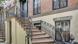 Una escalera con barandillas negras ornamentadas y peldaños color beige que conducen a una puerta con un ventanal encima.