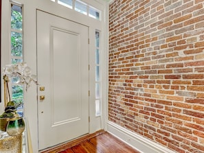 A room with a white door, a brick wall, and a wooden floor. - Gorgeous Designer Apartment, Heated Pool Access (Savannah)