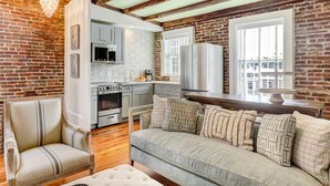 A cozy living room with a fireplace, a dining area, and a kitchen with modern appliances. - Gorgeous Designer Apartment, Heated Pool Access (Savannah)