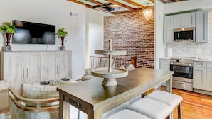 Una cocina moderna con pared de ladrillo, vigas de madera y una zona de comedor con mesa y banco de madera.