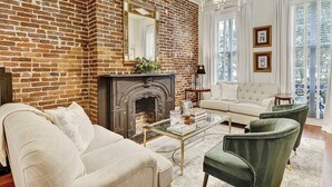 Una sala de estar con chimenea de ladrillo, un sofá, un sillón verde y una mesa de centro.