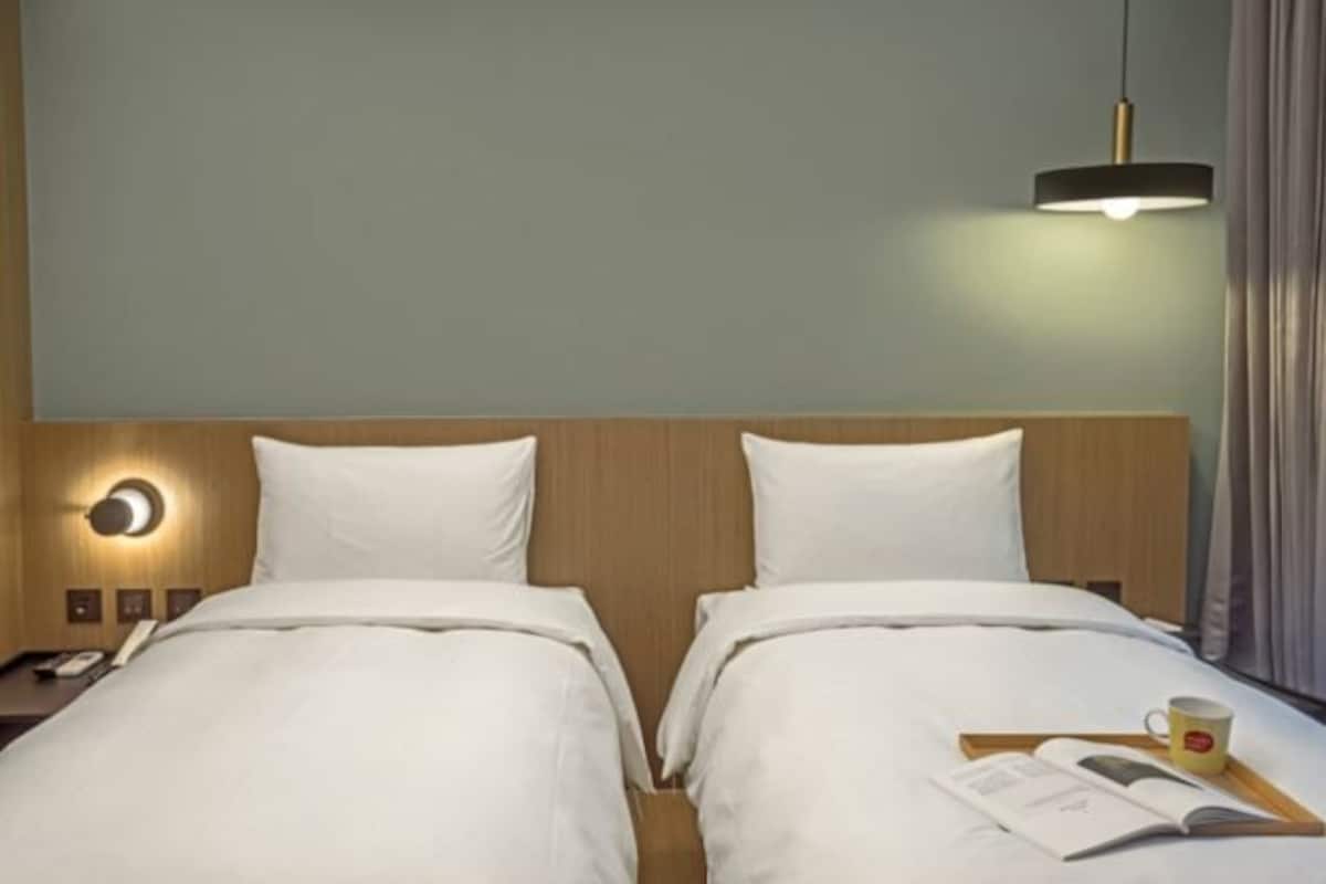Habitación de hotel con dos camas, una mesita de noche con lámpara, teléfono y bandeja con un libro y una taza.
