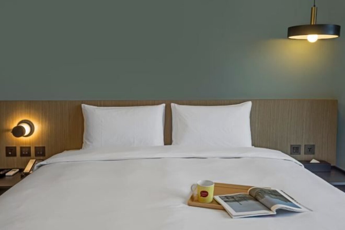 A neatly made bed with white linens, a bedside table with a lamp, and a tray with a mug and a book.