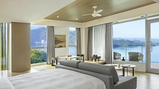 A hotel room with a large bed, a seating area with a table and chairs, and a balcony with a view of the mountains and lake. - Hotel Day Plus Sun Moon Lake (Yuchi)