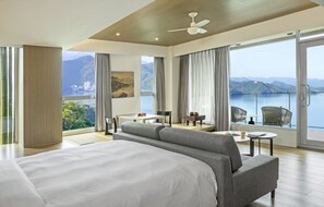 A hotel room with a large bed, a seating area with a table and chairs, and a balcony with a view of the mountains and lake. - Hotel Day Plus Sun Moon Lake (Yuchi)