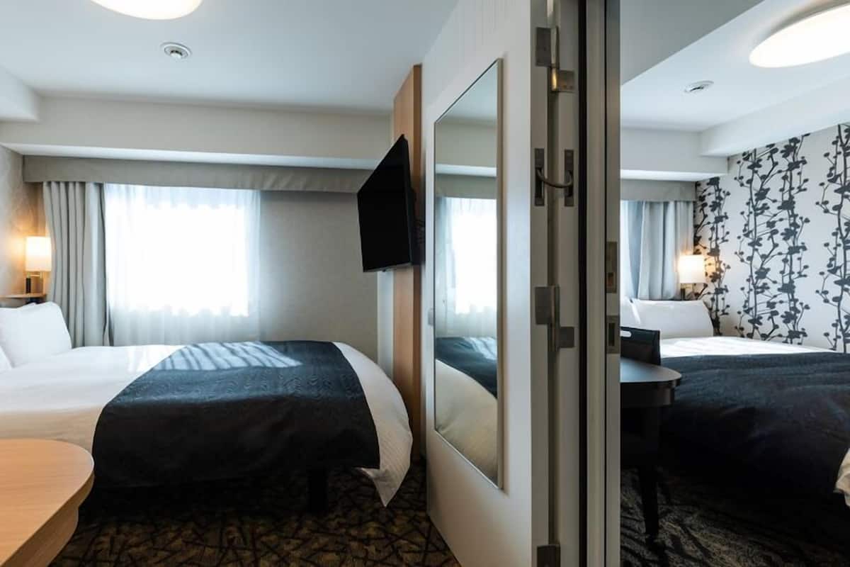 Hotellihuone, jossa on kaksi sänkyä, televisio, työpöytä ja peili.