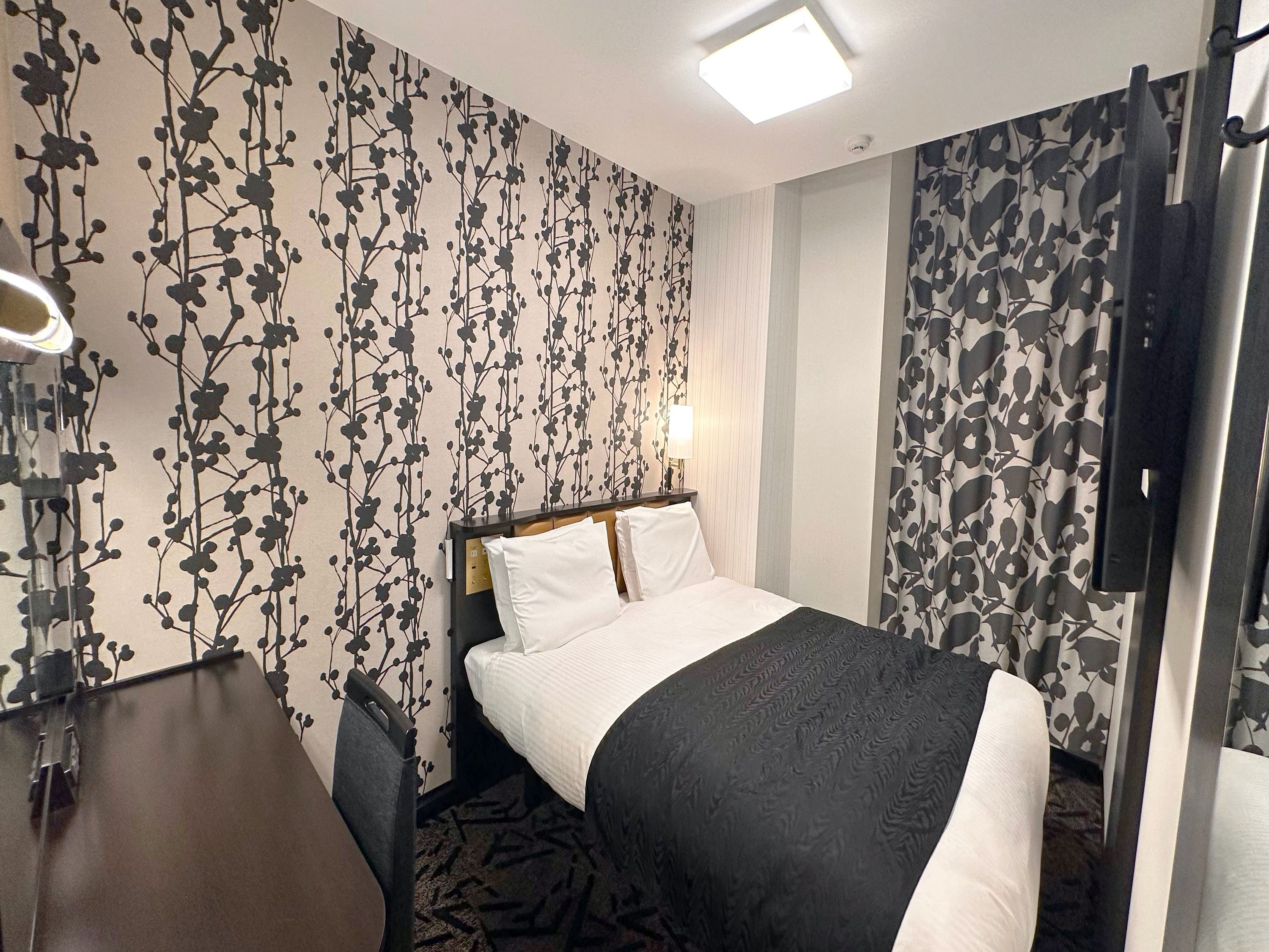 Una habitación de hotel con cama, escritorio, silla, televisor y pared con diseño.