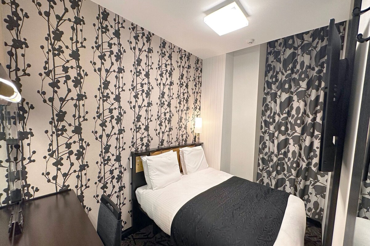 Ett hotellrum med en säng, ett skrivbord, en stol, en tv och en vägg med ett mönster.