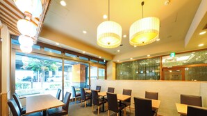 A restaurant interior with wooden tables and chairs, hanging pendant lights, and a view of the street outside. - APA Hotel Osaka Kadomashi Ekimae (Kadoma)