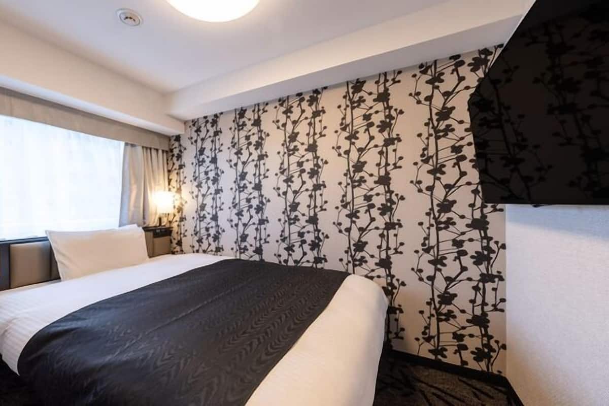 Une chambre d’hôtel avec un lit, un panneau de commande, une table de chevet, une lampe et un papier peint à motifs floraux.