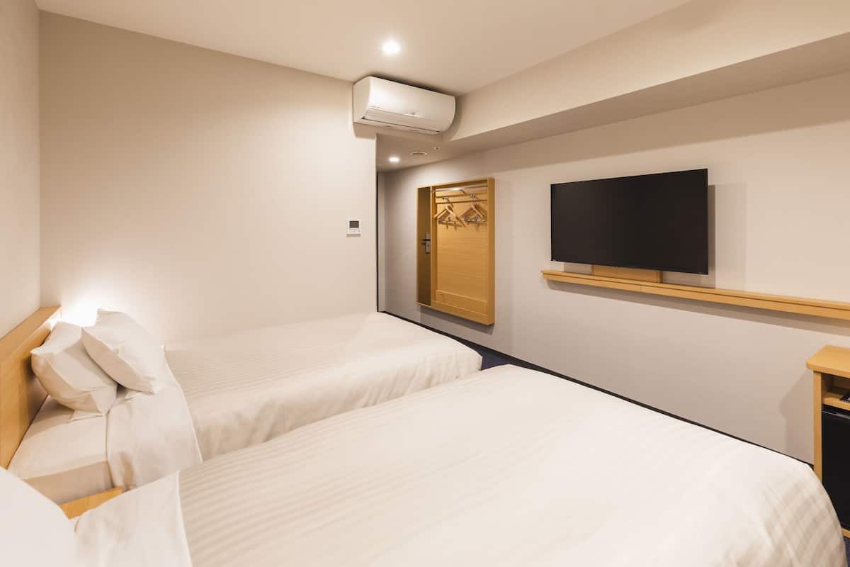 A hotel room with two single beds, a TV mounted on the wall, and a wooden wardrobe.