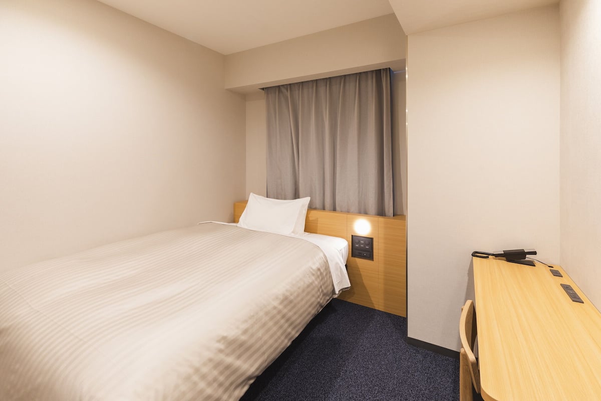 A hotel room with a bed, a desk, and a nightstand with a lamp.