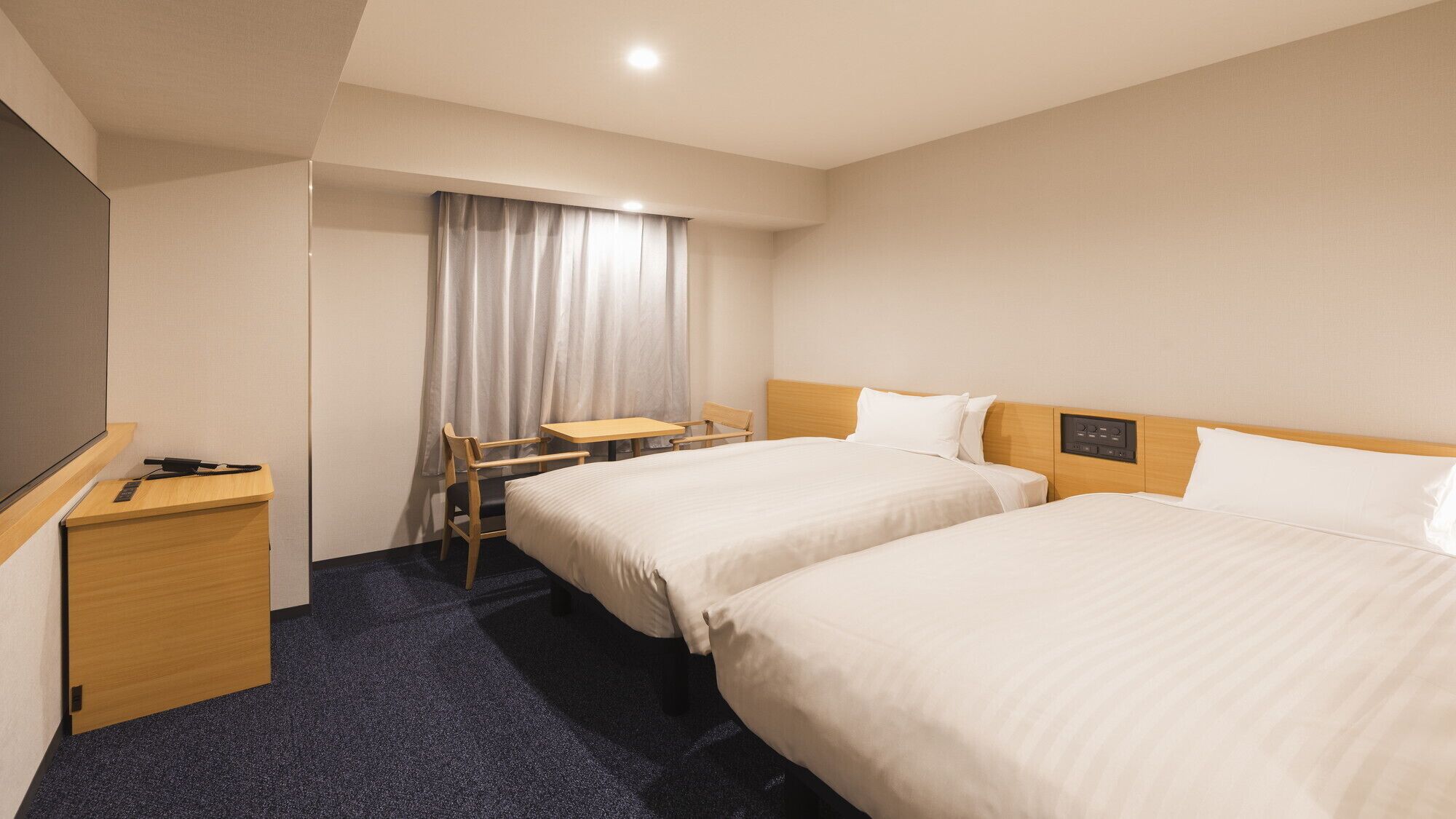 Habitación de hotel con dos camas, un escritorio, una silla, una mesita y un televisor.