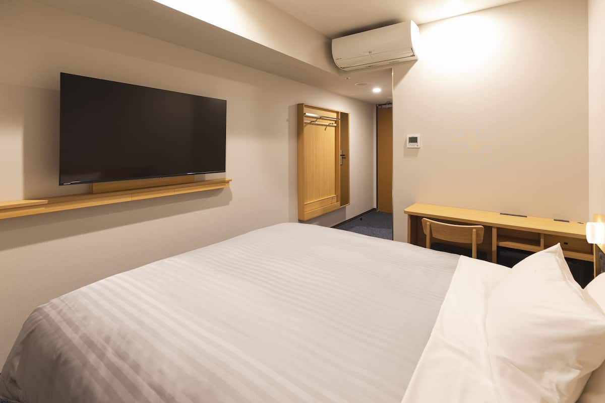 A hotel room with a bed, a TV mounted on the wall, a desk, and a chair.