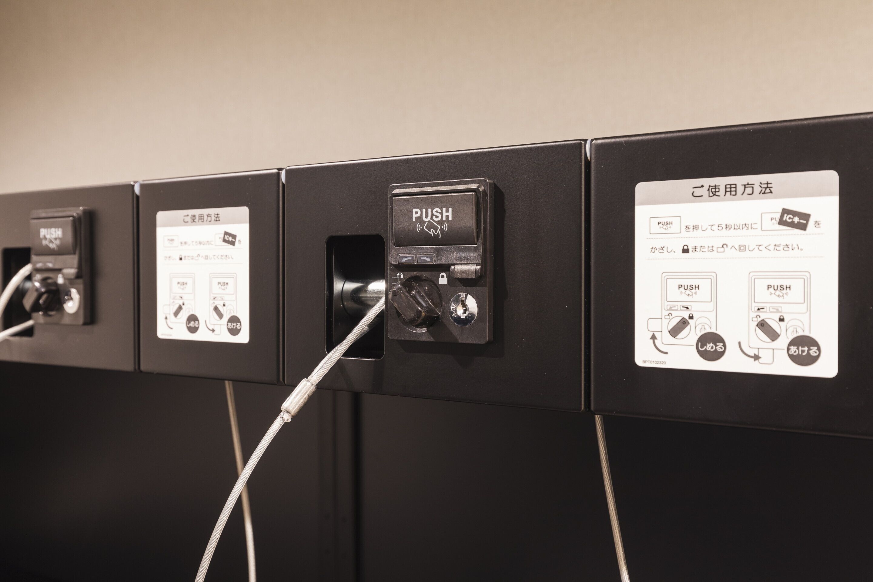 A row of black vending machines with push buttons and instructional labels in Japanese.