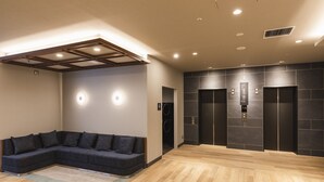 A modern lobby with a sectional sofa, wooden flooring, and two elevators. - Sotetsu Fresa Inn Daimon (Tokyo)