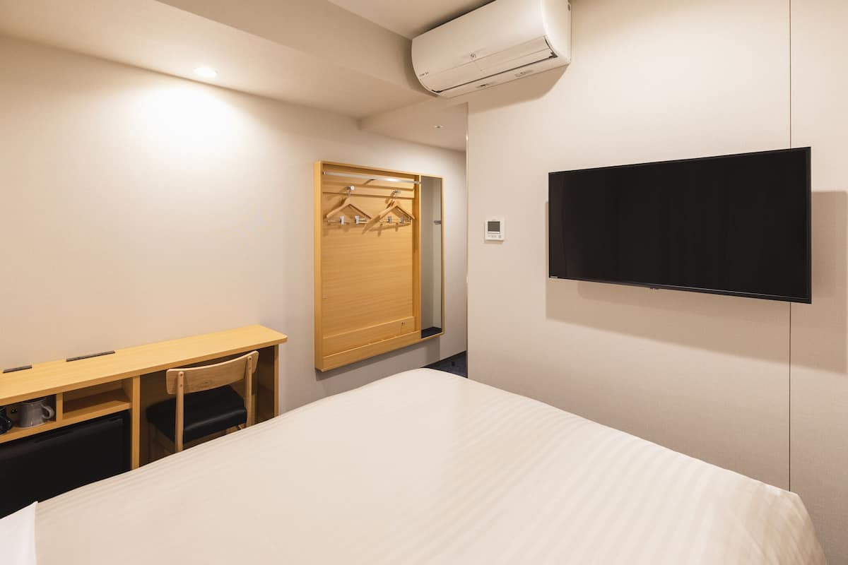 A hotel room with a bed, a desk, a chair, a TV, and a wardrobe with a mirror.