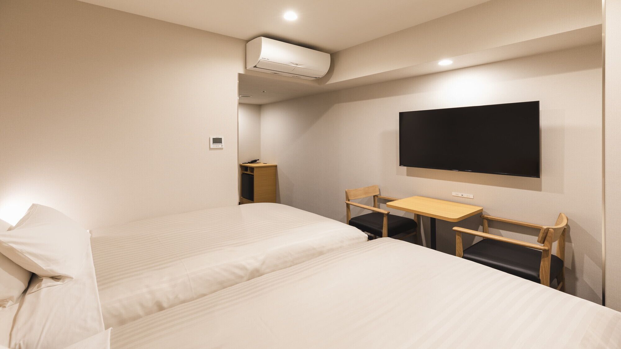 Habitación de hotel con dos camas, un escritorio, una silla, un televisor de pantalla plana y un equipo de aire acondicionado.