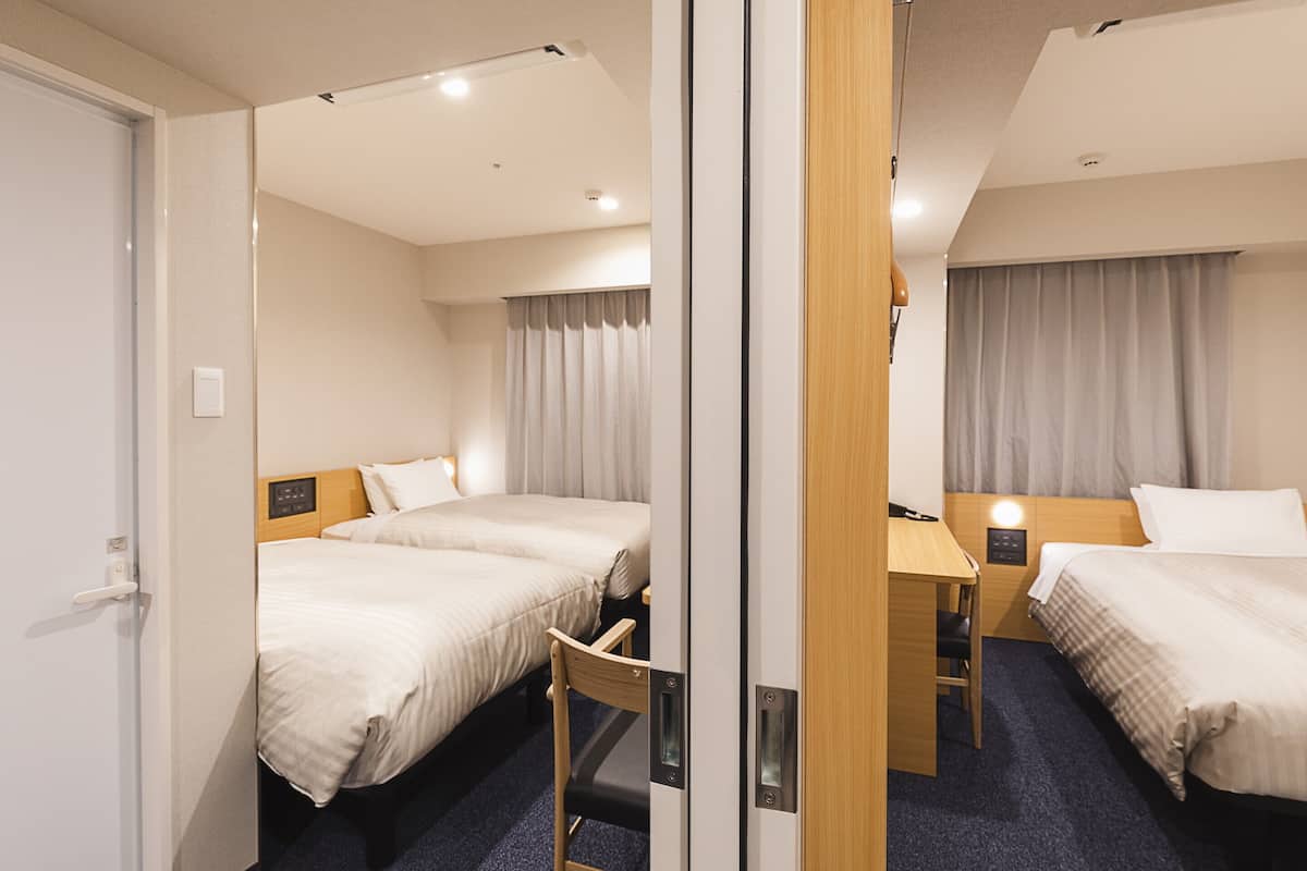 A hotel room with two beds, a desk, and a chair.