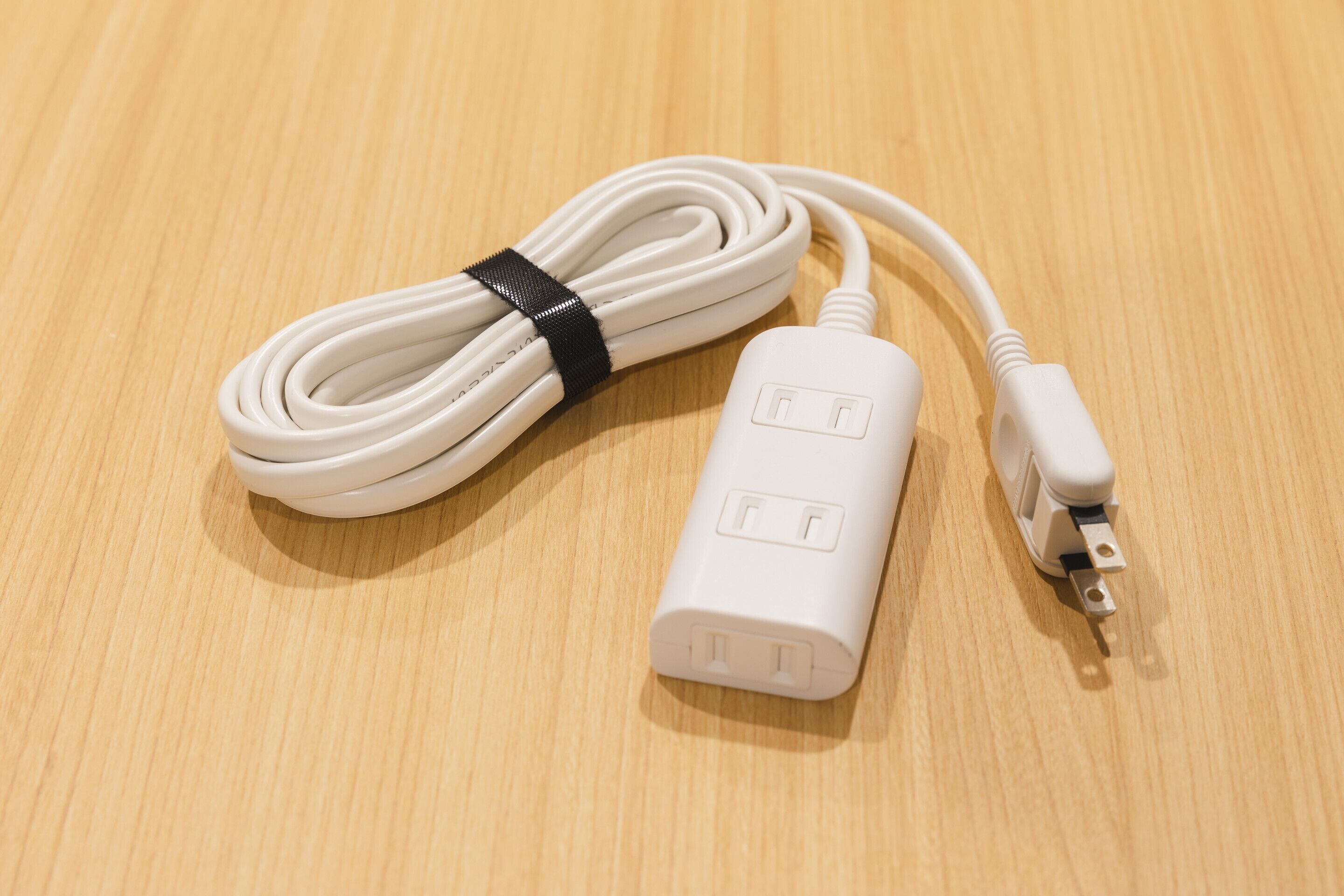 A white power strip with a black cable coiled around it, placed on a wooden surface.