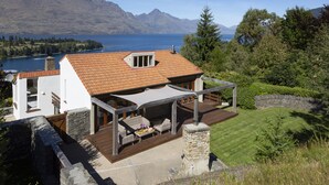 A modern house with a patio, stone walls, and a view of mountains and a lake.