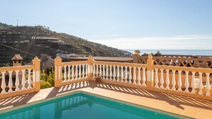 A swimming pool with a white balustrade, a view of a hillside, and a clear sky.