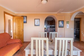 A dining area with a wooden table and chairs, a sofa, and a kitchen in the background.