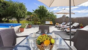 An outdoor dining area with a pool, lounge chairs, and a table set with fruit and wine glasses. - Villa "Manuel" with Mountain View, Sea View, Pool, Terrace & Garden (Nerja)