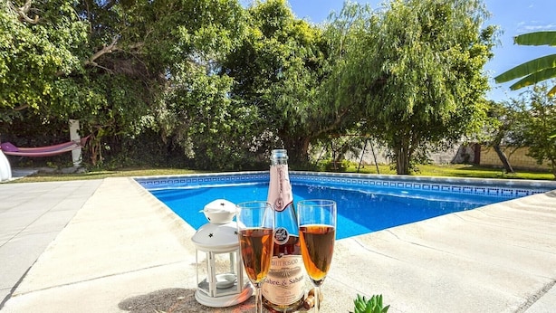 A poolside setting with a bottle of Brut Rosado wine, two glasses, a lantern, and a small potted plant. - Villa "Manuel" with Mountain View, Sea View, Pool, Terrace & Garden (Nerja)