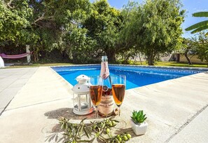 A poolside setting with a bottle of Brut Rosado wine, two glasses, a lantern, and a small potted plant.