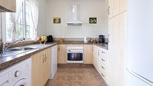 A kitchen with a sink, stove, and oven, wooden cabinets, and a window with curtains. - Villa "Manuel" with Mountain View, Sea View, Pool, Terrace & Garden (Nerja)