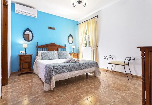 A bedroom with a bed, two bedside tables, a mirror, a window with curtains, and a chair.