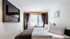 Ein Hotelzimmer mit einem Bett, einem an der Wand montierten Fernseher, einem Fenster mit Vorhängen und einem gerahmten Bild.