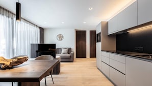 Eine moderne Küche mit Backofen, eine Essecke mit Holztisch und Stühlen sowie ein Wohnzimmer mit Sofa und Fernseher.