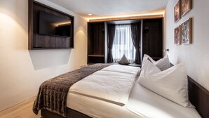Ein Hotelzimmer mit Bett, einem Wandfernseher, einem Fenster mit Vorhängen und Bildern an der Wand.