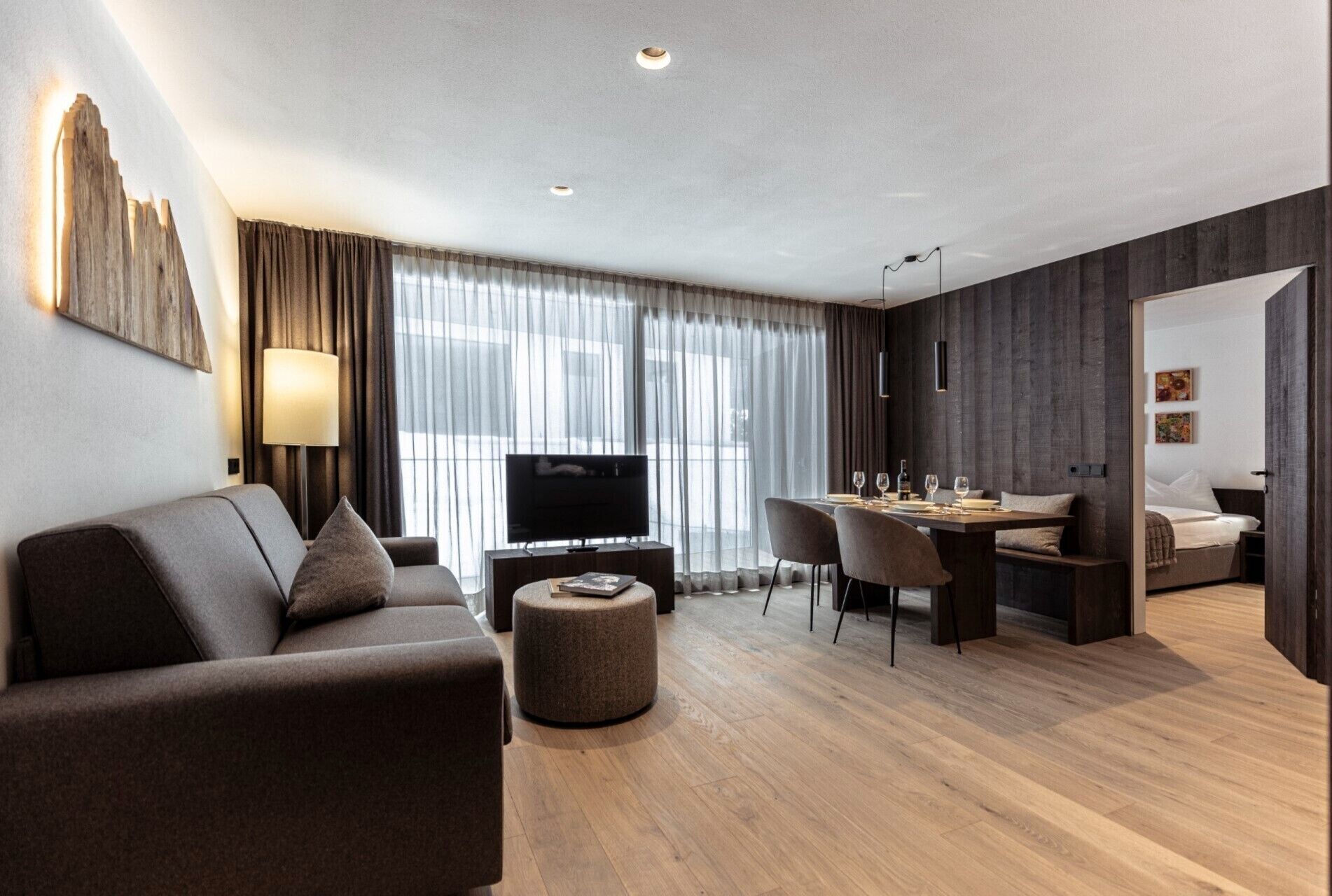 A modern hotel room with a sofa, TV, dining area, and a bed.