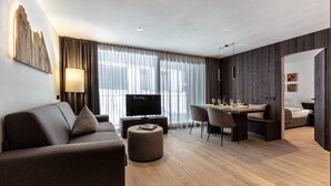Ein modernes Hotelzimmer mit Sofa, Fernseher, Essbereich und Bett.