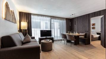 A modern hotel room with a sofa, TV, dining area, and a bed.