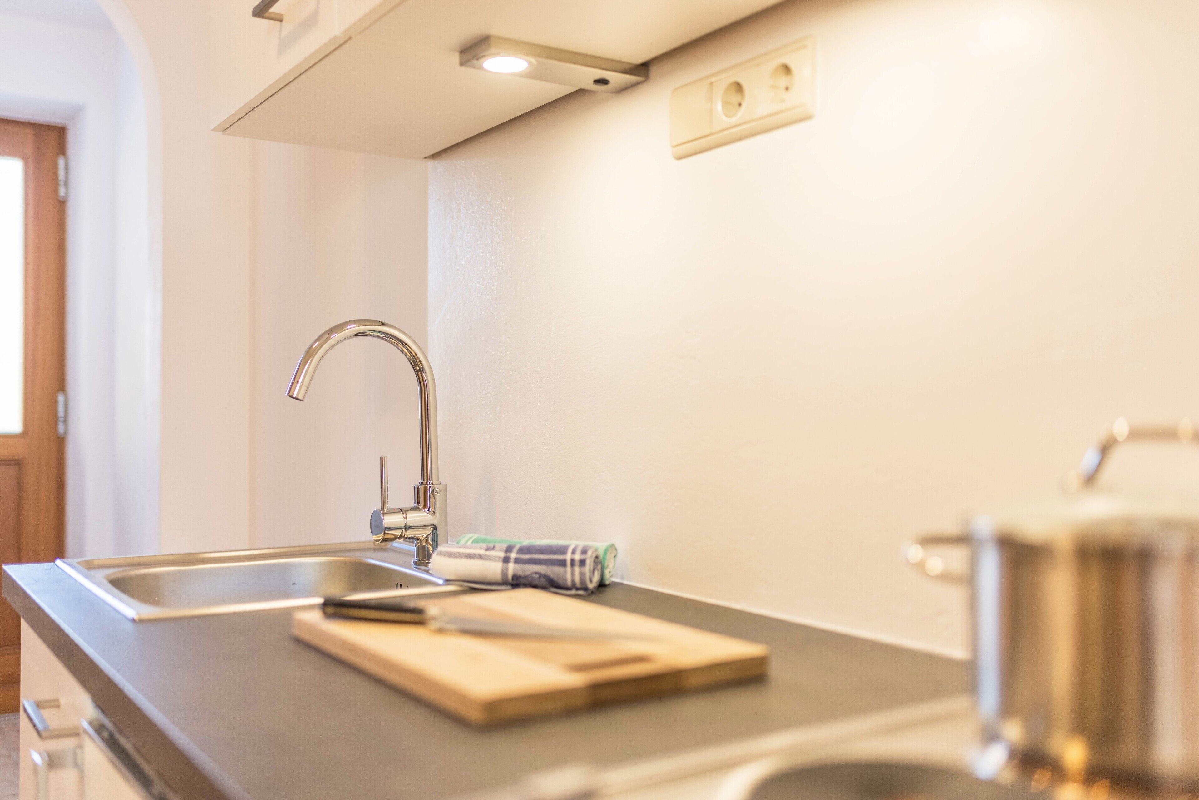 A kitchen with a stainless steel sink, a wooden cutting board, and a rolled-up towel.