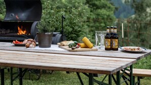 A wooden picnic table with food, a grill, and beer bottles. - Lettnerhof – Family Suite Balcony 5. Surrounded by Nature, South-Facing Balcony, Mountain View, Wi-Fi. (Welsberg)